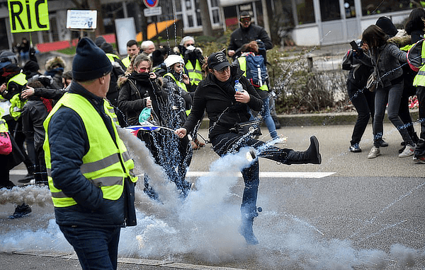 A woman yellow vest protester kicks a smoke bomb, January 2019.